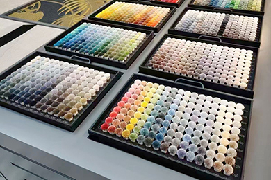 Nuancier tapis touffé sur mesure: Plusieurs sets de pompons de fils pour tapis sur mesure disposés sur un bureau gris, montrant différentes couleurs vives pour designs personnalisés