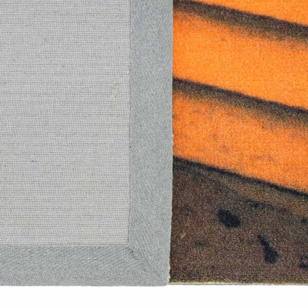 Un tapis en polyester imprimé sur mesure dont le dos est recouvert d'un tissu gris clair et d'un ruban adhésif, à côté d'un motif rayé orange et marron vibrant.